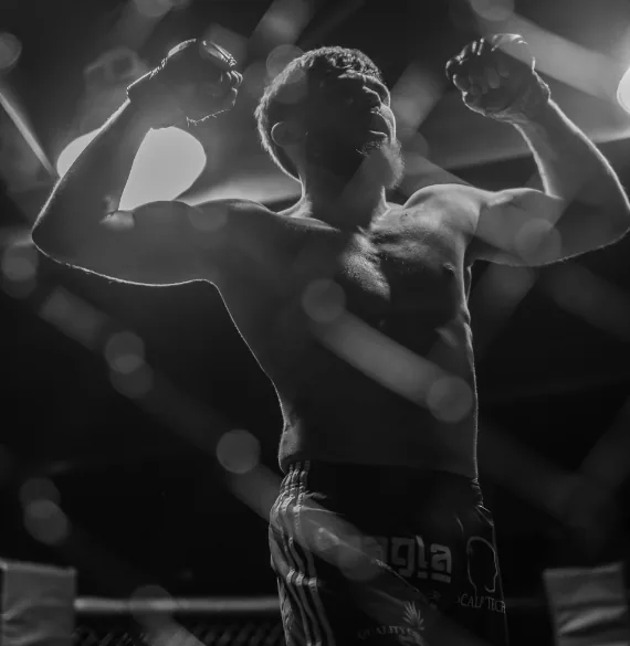 A fighter with both arms raised in the cage after a win, shot in black and white