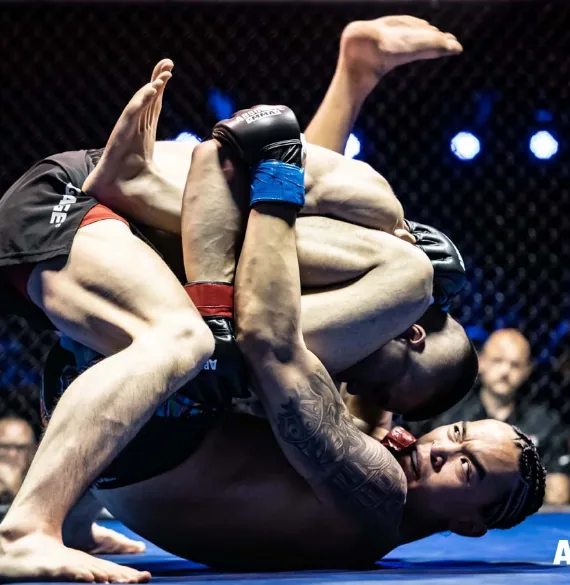 Two fighters in a grappling exchange on the mat, one working for a submission